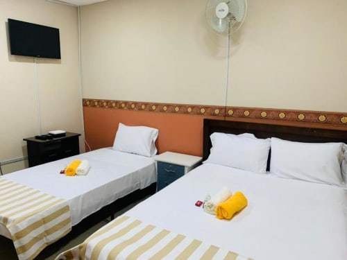 Camas gemelas con sábanas blancas en el hotel Casa Mango de Cali, Colombia. La habitación cuenta con cabecera naranja y ventilador de pie.