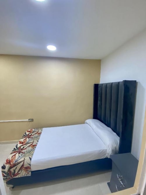 Habitación moderna del hotel Casa Mango en Cali con cabecera oscura, ropa de cama blanca y pared de acento amarilla