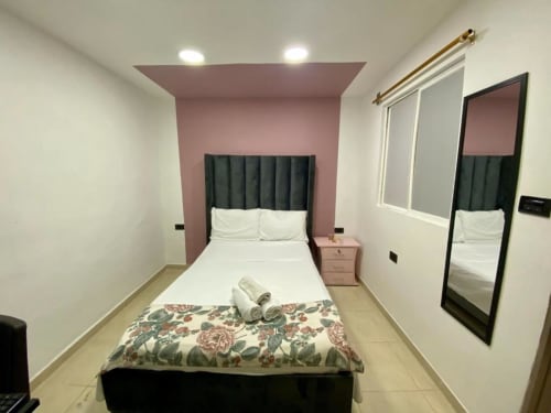 Habitación moderna en el hotel Casa Mango de Cali con pared de acento rosa, cabecero oscuro, ropa de cama blanca y espejo.