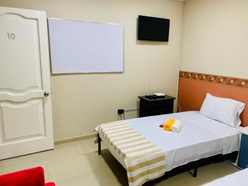 Habitación del hotel Casa Mango en Cali con cama, cabecero naranja, camino de cama a rayas amarillas, TV y pizarra