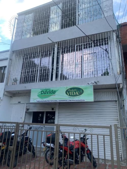 Edificio blanco de dos pisos con ventanas enrejadas en Cali, Colombia. Tienda en planta baja con productos verdes Davida Vida