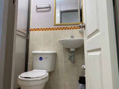 Baño moderno del hotel Casa Mango en Cali con accesorios blancos, azulejos beige y cenefa de mosaico rojo-amarillo