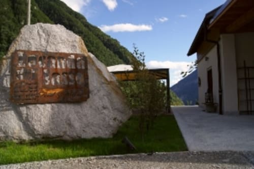 Eingang der Zimmer der Locanda del Sasso in Crodo mit rustikalem Steinschild, modernem Gebäude und Bergblick