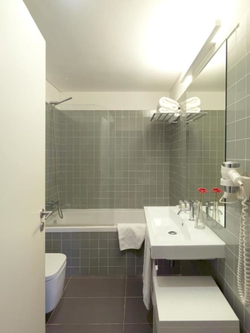 Modern bathroom in Studio Apartment at New Oporto Apartments, Porto, with green tiles, shower, sink, toilet, and towel rack.