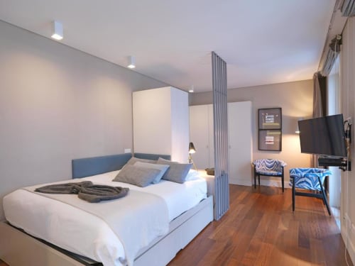 Modern studio apartment bedroom at New Oporto Apartments in Porto, featuring a bed with blue headboard, TV, wooden flooring,