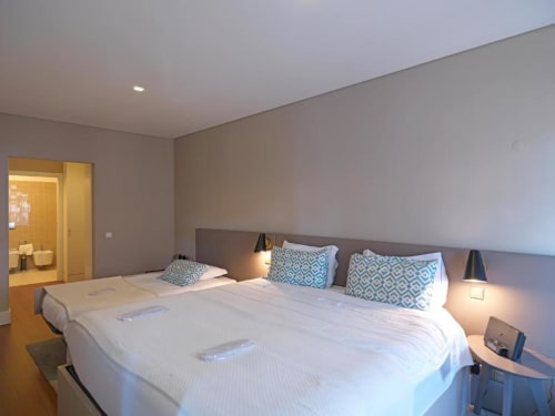 Modern bedroom in Porto apartment with twin beds, blue patterned pillows, ensuite bathroom, and city views