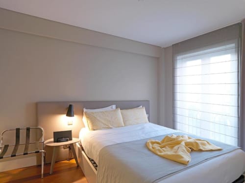 Modern bedroom in New Oporto Deluxe Apartment with queen bed, yellow accents, wooden floors, and bright window in Porto