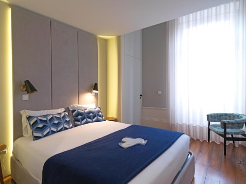 Dormitorio moderno en New Oporto Apartments, Porto, con ropa de cama azul, iluminación ambiental y muebles contemporáneos
