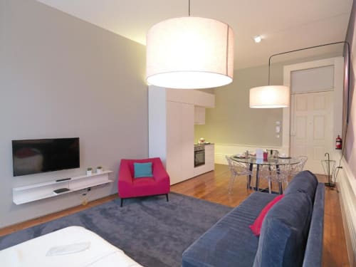 Modern Deluxe Apartment living area at New Oporto Apartments, Porto with pink armchair, gray sofa, flat-screen TV, and open