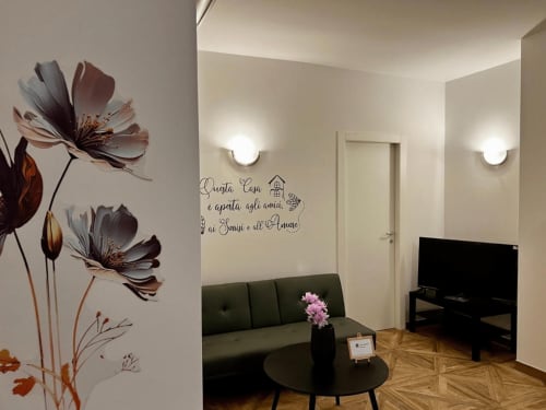 Stilvolles Wohnzimmer im EmilBo' House mit Blumenwandkunst, dunklem Sofa, schwarzem TV-Ständer und einladender italienischer Einrichtung