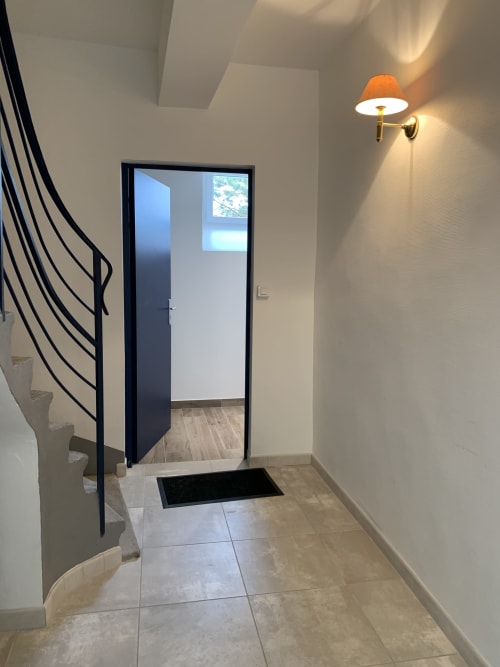 Entrée contemporaine du Restaurant du Port avec porte à cadre noir, sol carrelé, escalier en spirale et applique murale orange