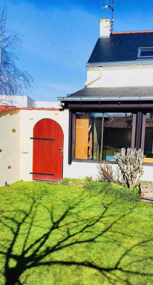 Gîte Conciergerie Pour Tous à Darazac avec porte rouge, extension moderne et vue sur jardin verdoyant