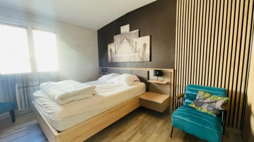 Chambre moderne du gîte Conciergerie Pour Tous By Patty à Darazac avec lit en bois, fauteuil turquoise et vue sur le jardin