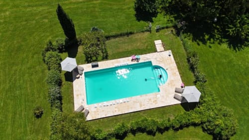 Vue aérienne de la piscine turquoise avec patio en pierre, chaises longues et jardins luxuriants du gîte Les Papillons de Baccara