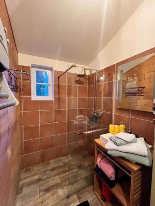 Salle de bain moderne avec douche en carrelage terracotta, meuble vasque en bois et fenêtre au gîte Les papillons de baccara à Gondrin