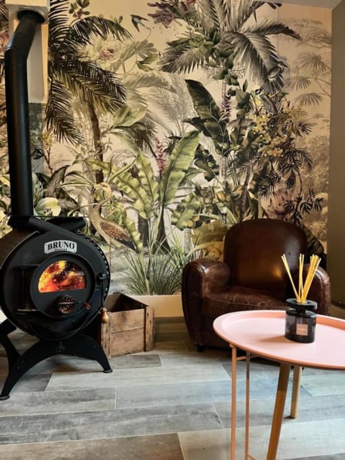 Lounge Les papillons de baccara avec poêle en bois noir, fauteuil en cuir marron, papier peint tropical et table d'appoint moderne.