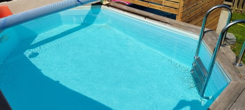 Piscine aux eaux cristallines à la Résidence des dunes B&B à Landéda, France avec échelle métallique et terrasse en bois