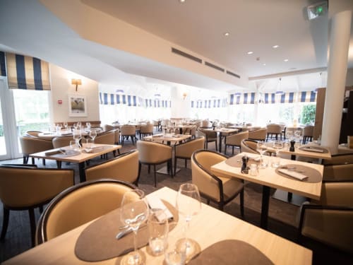Elegant dining room at Le Prieuré Du Preux with tan leather chairs, blue-striped windows, and natural light in Sépeaux Saint