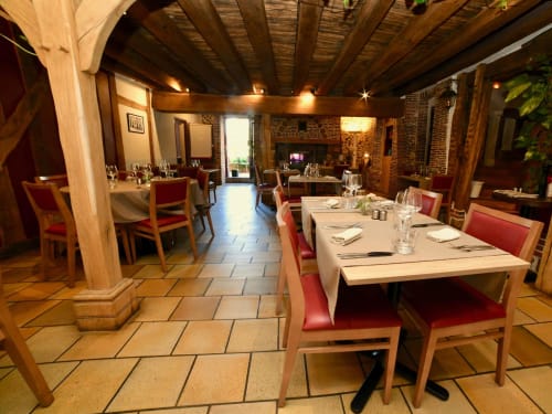 Elegant dining room at Le Prieuré Du Preux with wooden beams, brick fireplace, and set tables with red chairs in Sépeaux