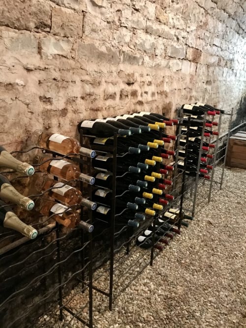 Wine bottles stored in black racks against stone cellar wall at Les Maisons de Chamirey, Mercurey