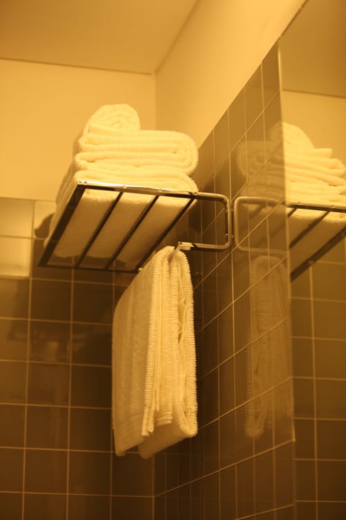 Bathroom shelf with neatly folded white towels and hanging towels in New Oporto Apartments, Porto