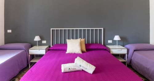 Bright magenta and purple beds in C'era una Volta Deluxe Quadruple Room in Palermo with white nightstands and garden view