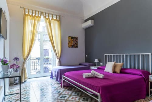 Luxurious Deluxe Quadruple Room at C'era una Volta in Palermo with magenta beds, yellow curtains, dark accent wall, and