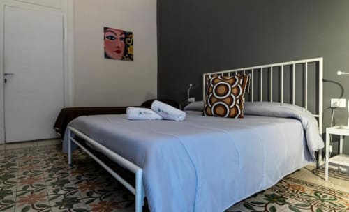 Camera spaziosa in un bed & breakfast a Palermo con letto a struttura metallica bianca, biancheria azzurra, tappeti decorativi e arte contemporanea