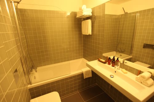 Modern bathroom at New Oporto Apartments in Porto with tiled walls, bathtub, shower, vanity sink, and toiletries on counter