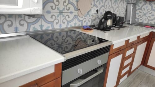 Cocina moderna con placa de inducción, encimeras blancas, azulejos decorativos azules y gabinetes de madera en Casa Torrens