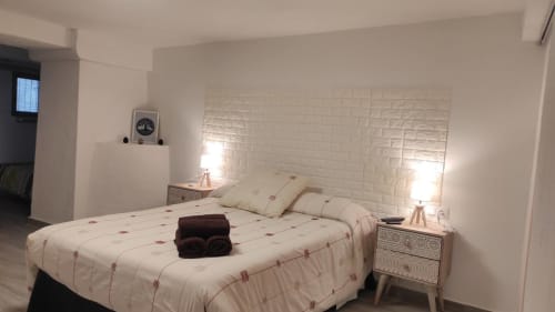 Dormitorio moderno en Casa Torrens con cabecero de ladrillo blanco, ropa de cama crema, lámparas gemelas y mesitas de noche de madera en Polop de la