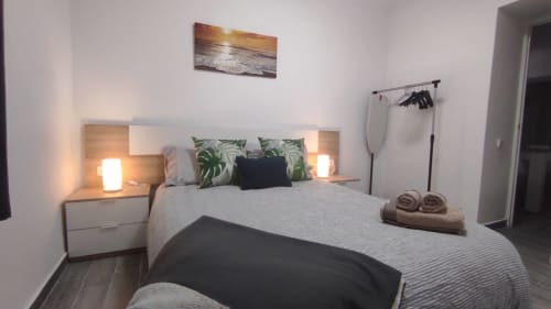 Dormitorio moderno en Casa Torrens con cama, cojines botánicos verdes, lámparas de mesita y arte costero en Polop de la Marina