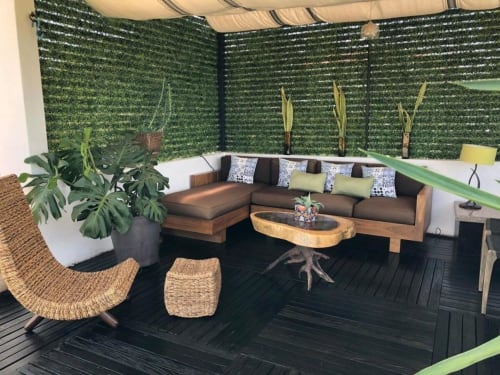 Moderna sala de estar en Alojamientos Zoogocho con sofá seccional marrón, sillas de mimbre y pared de follaje artificial verde