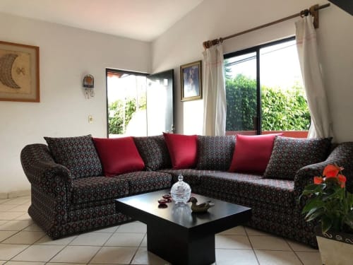 Moderno salón en Casa El Nogal de Alojamientos Zoogocho con sofá seccional estampado, cojines rojos y amplios ventanales