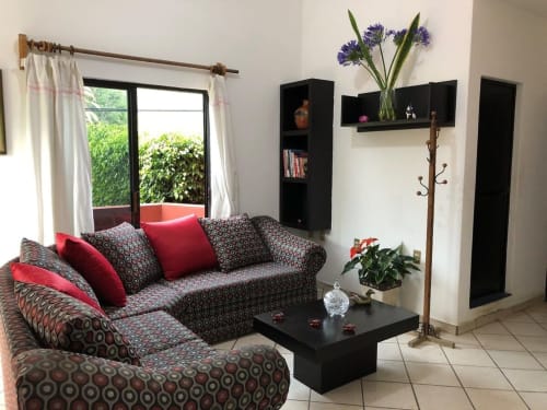 Modern living room at El Nogal House in San Andrés Huayapam with patterned sofa, red pillows, black shelving, and garden view