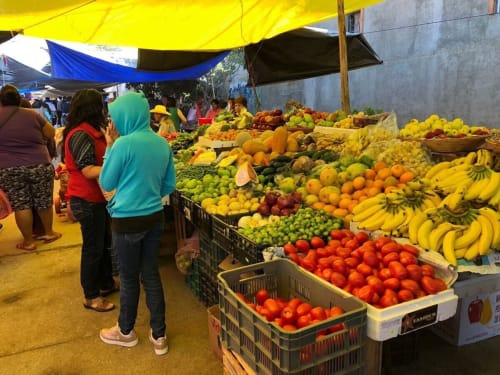 Vibrant outdoor market in San Andrés Huayapam with colorful produce including bananas, tomatoes, and citrus fruits displayed
