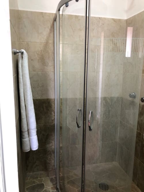 Cabina de ducha de vidrio con muros de azulejos oscuros y accesorios cromados en el Apartamento Zeus 12 de Alojamientos Zoogocho, San Andrés