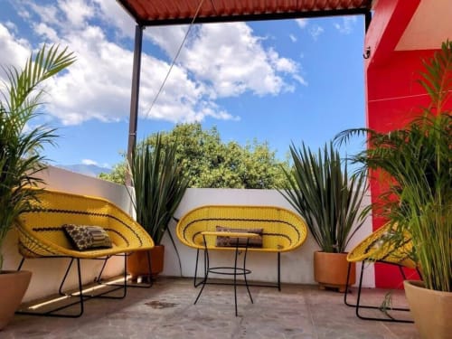 Patio soleado del Apartamento Zeus 12 en San Andrés Huayapam con sillas tejidas amarillas, plantas en macetas y pared roja