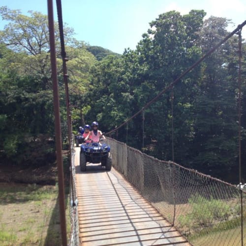 Guests riding ATV on wooden bridge through lush forest canopy at Villa Mango B&B, Nosara