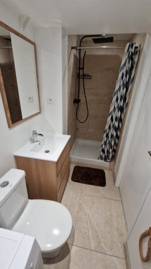 Salle de bain moderne avec toilettes, vanité en bois, miroir et douche à l'italienne avec robinetterie noire et rideau motifs