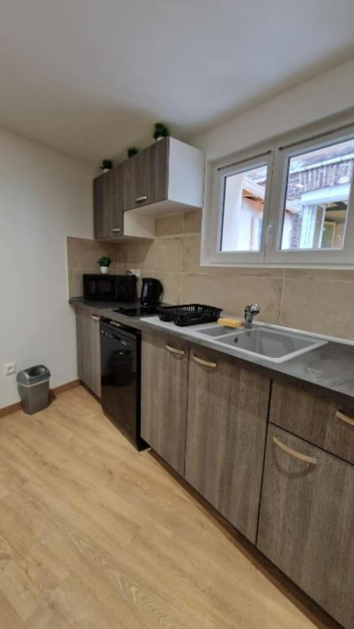 Cuisine moderne avec armoires en bois, cuisinière noire, évier et plan de travail dans un appartement à louer à Pont-Sainte-Maxence