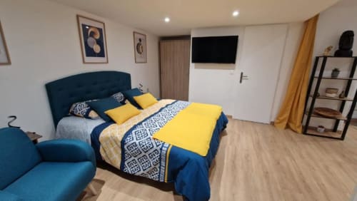Chambre moderne avec lit bleu rembourré, literie jaune, téléviseur et rangements à Location Saisonnière Pont-Sainte-Maxence