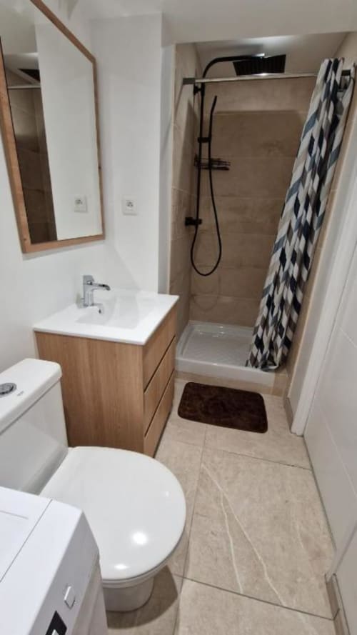 Salle de bain moderne de l'appartement Pont-Sainte-Maxence avec meuble vasque en bois, toilettes blanches, douche, miroir et serviette géométrique