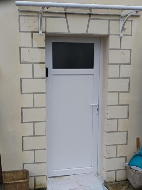 Porte d'appartement blanche avec fenêtre et imposte, encadrement en brique, location saisonnière à Pont-Sainte-Maxence