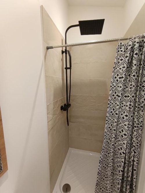 Douche moderne avec pommeau de douche effet pluie noir, paroi vitrée transparente et rideau à motifs dans la salle de bains d'un appartement