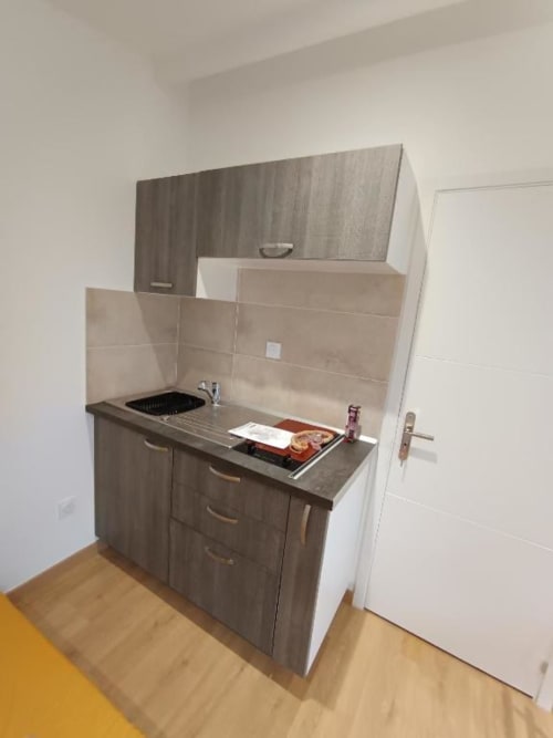 Petite kitchenette dans un appartement à Pont-Sainte-Maxence avec armoires grises, cuisinière et dosseret en carrelage beige