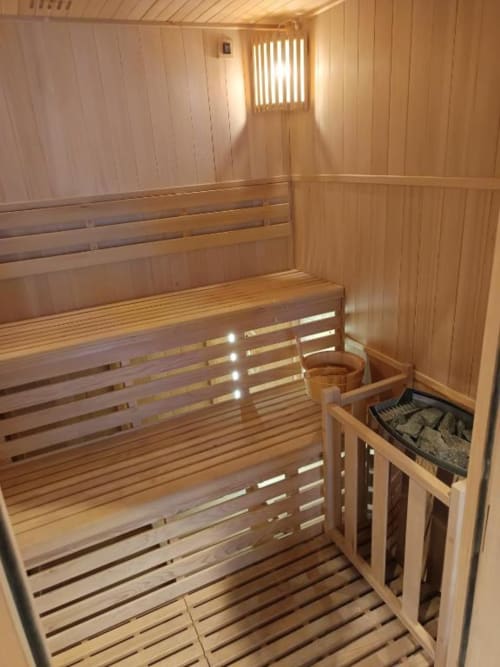 Intérieur de sauna moderne avec bancs en bois, éclairage LED et poêle en pierre à la villa de Pont-Sainte-Maxence