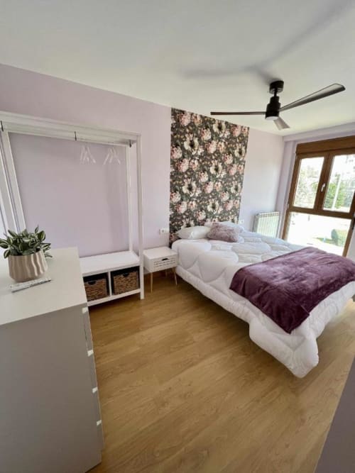 Dormitorio moderno en AlmaMaterSalamanca con paredes púrpuras, detalle floral, ropa de cama blanca, piso de madera y puertas de cristal