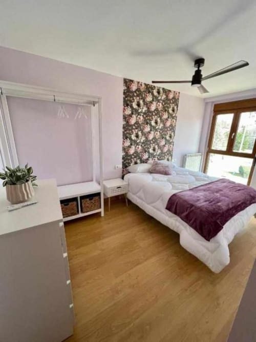 Dormitorio moderno en apartamento AlmaMaterSalamanca con paredes púrpura, papel tapiz floral, suelos de madera y ventilador de techo
