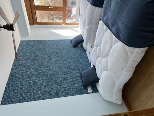 Felpudo azul texturizado en la entrada de Apartamentos AlmaMaterSalamanca con puerta de madera y vista a la ventana